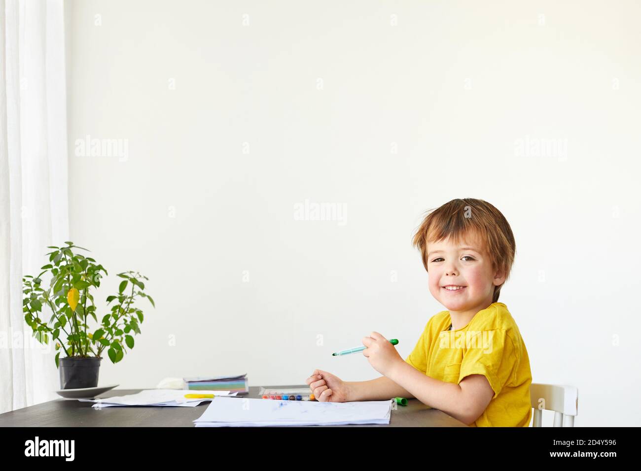 Sorridente ragazzino al tavolo disegnare con i pastelli sopra bianco Foto Stock