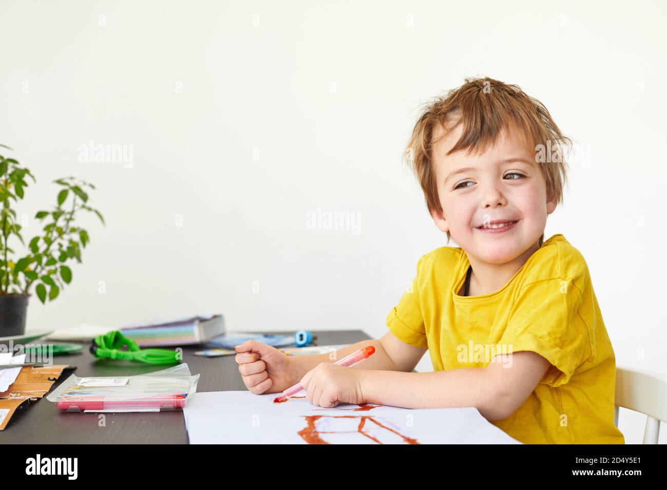 Sorridente ragazzino al tavolo disegnare con i pastelli sopra bianco Foto Stock