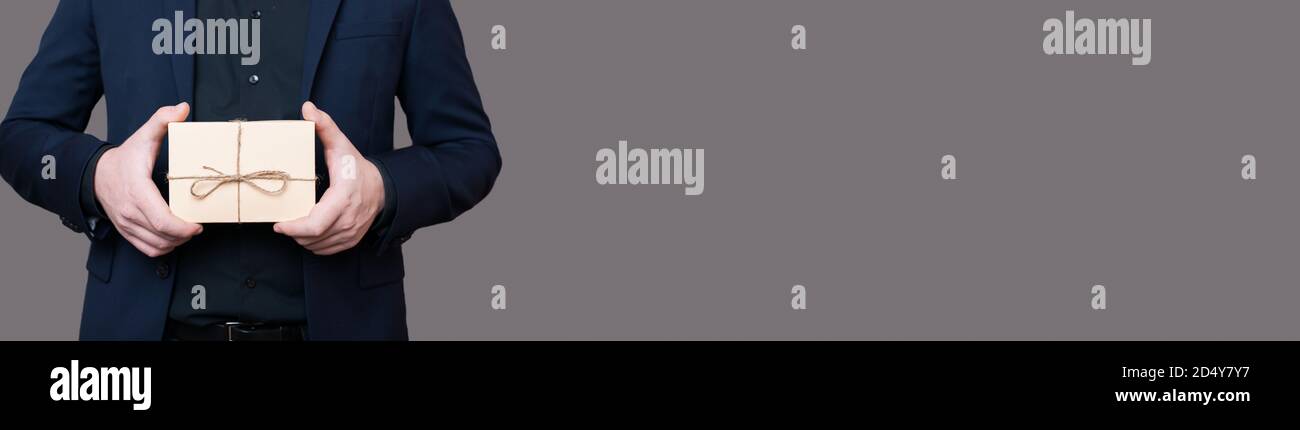 L'uomo caucasico nel seme sta tenendo un presente nelle mani posa senza faccia su una parete grigia con spazio libero Foto Stock