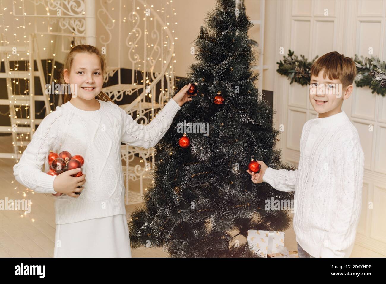 I bambini decorano l'albero di Natale in un interno luminoso. Ragazza e ragazzo, fratello e sorella appendono i giocattoli di Capodanno sui rami di abete rosso. Concetto di Natale e Capodanno per la famiglia. Foto Stock