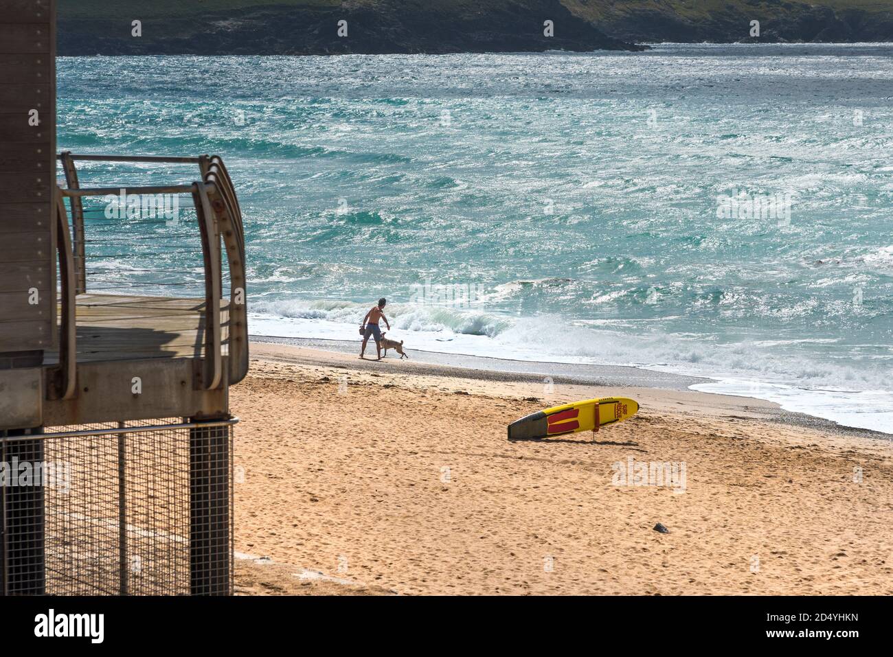 Un uomo che lancia una palla per il suo cane al sole della mattina presto sulla spiaggia di Fistral a Newquay in Cornovaglia. Foto Stock