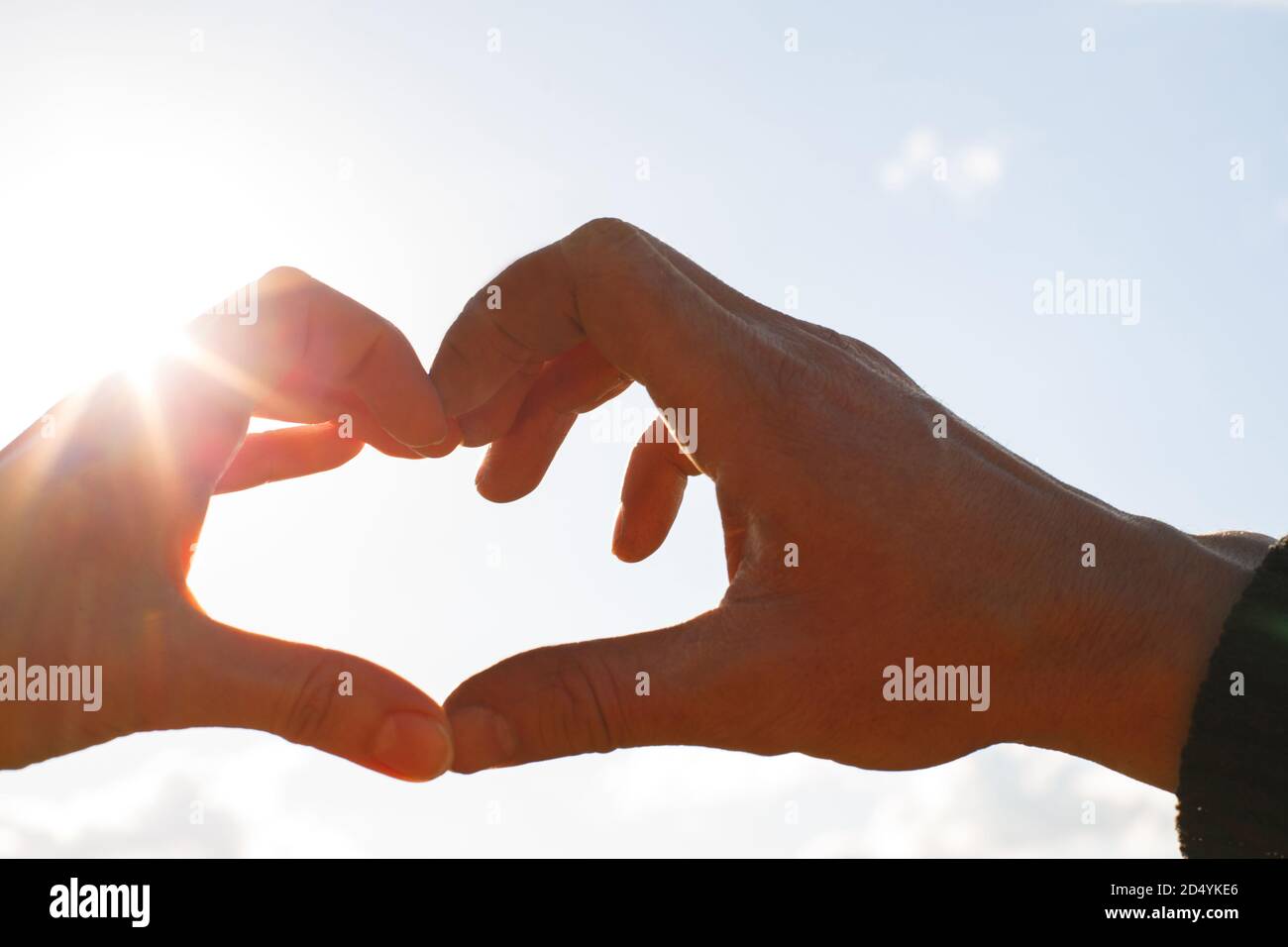 Due mani, maschio e femmina, sono unite a forma di cuore contro il cielo con i raggi del sole all'apertura. Simbolo di una coppia innamorata, Valenti Foto Stock