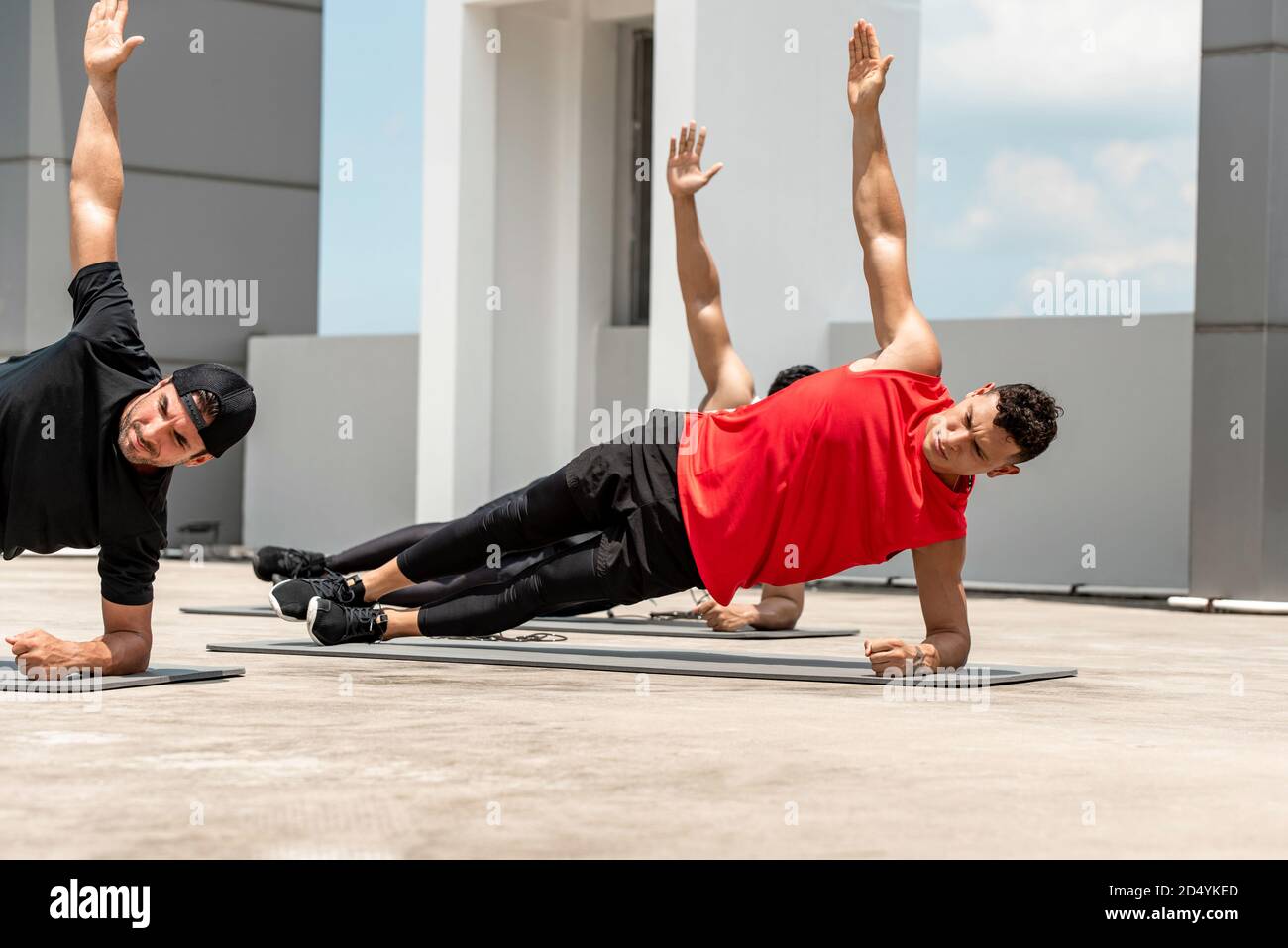 Gruppo di uomini atletici facendo laterale tavola mattina esercizio di allenamento all'aperto sul tetto Foto Stock