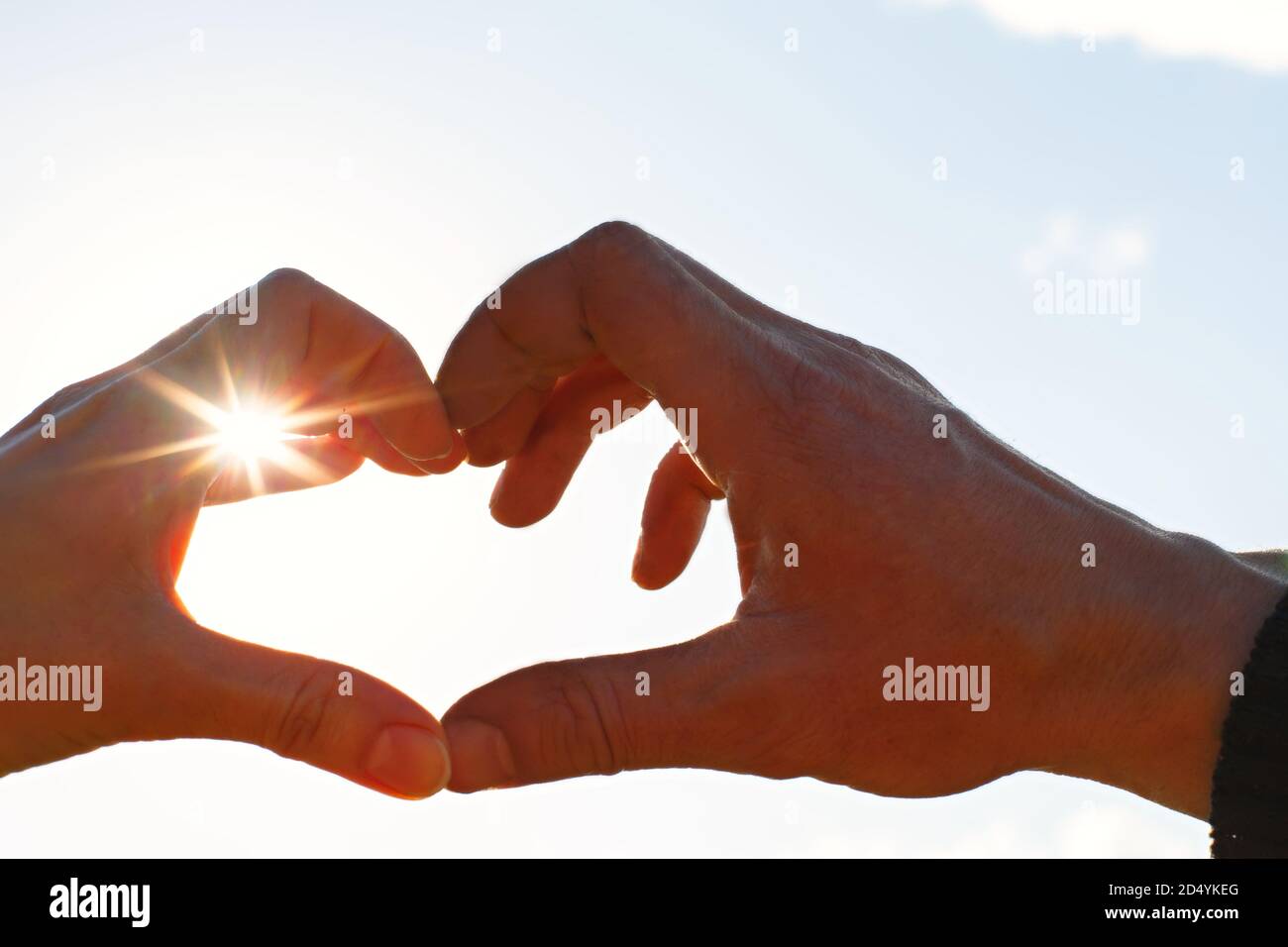 Due mani, maschio e femmina, sono unite a forma di cuore contro il cielo con i raggi del sole all'apertura. Simbolo di una coppia innamorata, Valenti Foto Stock