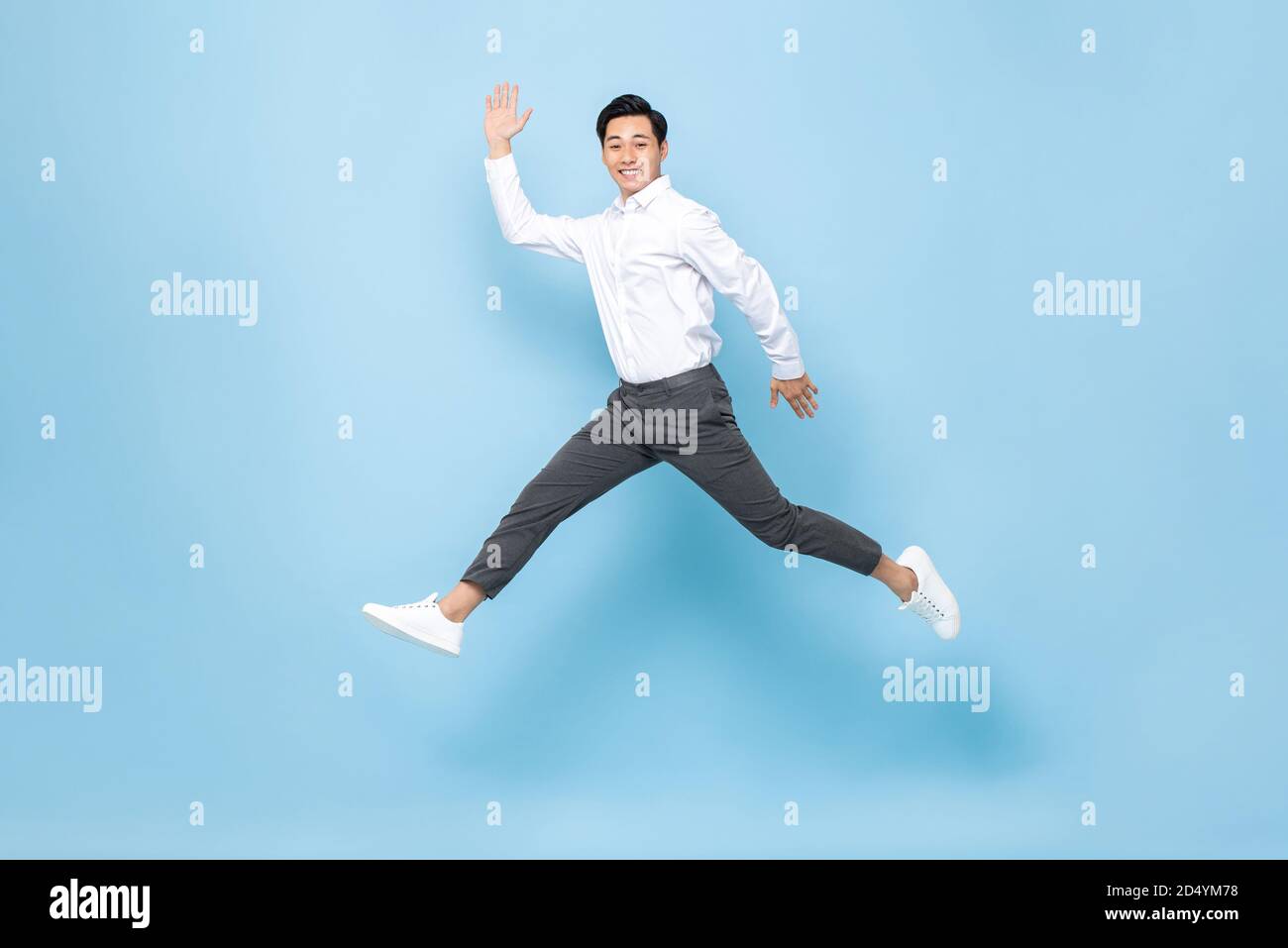 Ritratto a lunghezza intera di felice sorridente energico asiatico uomo in abiti semi-formali che saltano in aria media isolati sulla luce sfondo blu Foto Stock