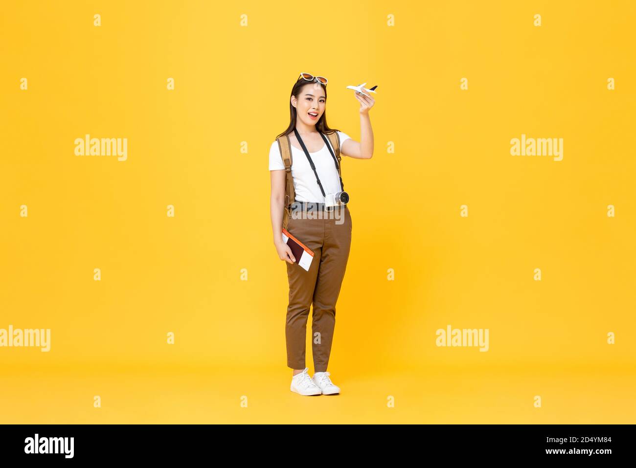 Ritratto di viaggio sorridente giovane bella donna turistica asiatica tenuta modello di aereo e passaporto isolati su sfondo giallo studio Foto Stock