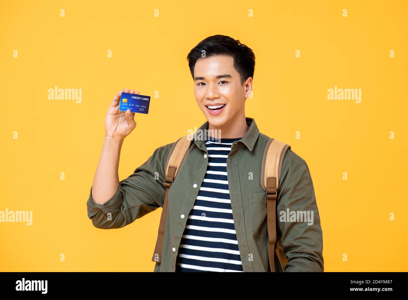 Vita in su ritratto di sorridente giovane asiatico zaino in spalla turista uomo mostra carta di credito in studio isolato sfondo giallo Foto Stock