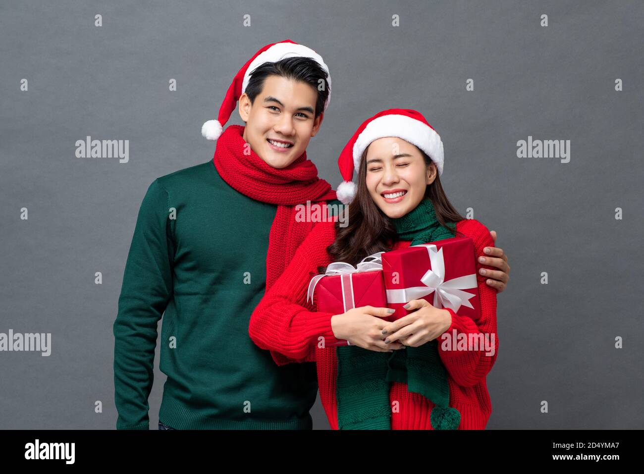 Sorridente felice coppia asiatica in colorato rosso e verde Natale vestiti con scatole regalo su sfondo grigio isolato Foto Stock