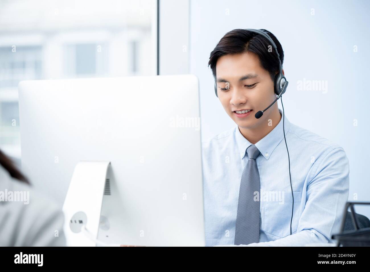 Bello sorridente maschio Asiatico telemarketing personale che indossa microfono cuffie di lavoro nel call center Foto Stock