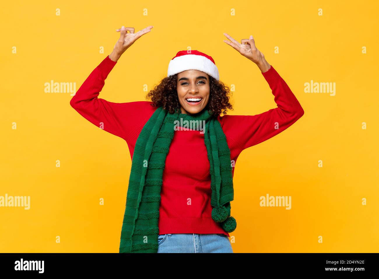 Allegra donna felice in abbigliamento di Natale sorridente e alzando le mani su in giallo studio isolato sfondo Foto Stock