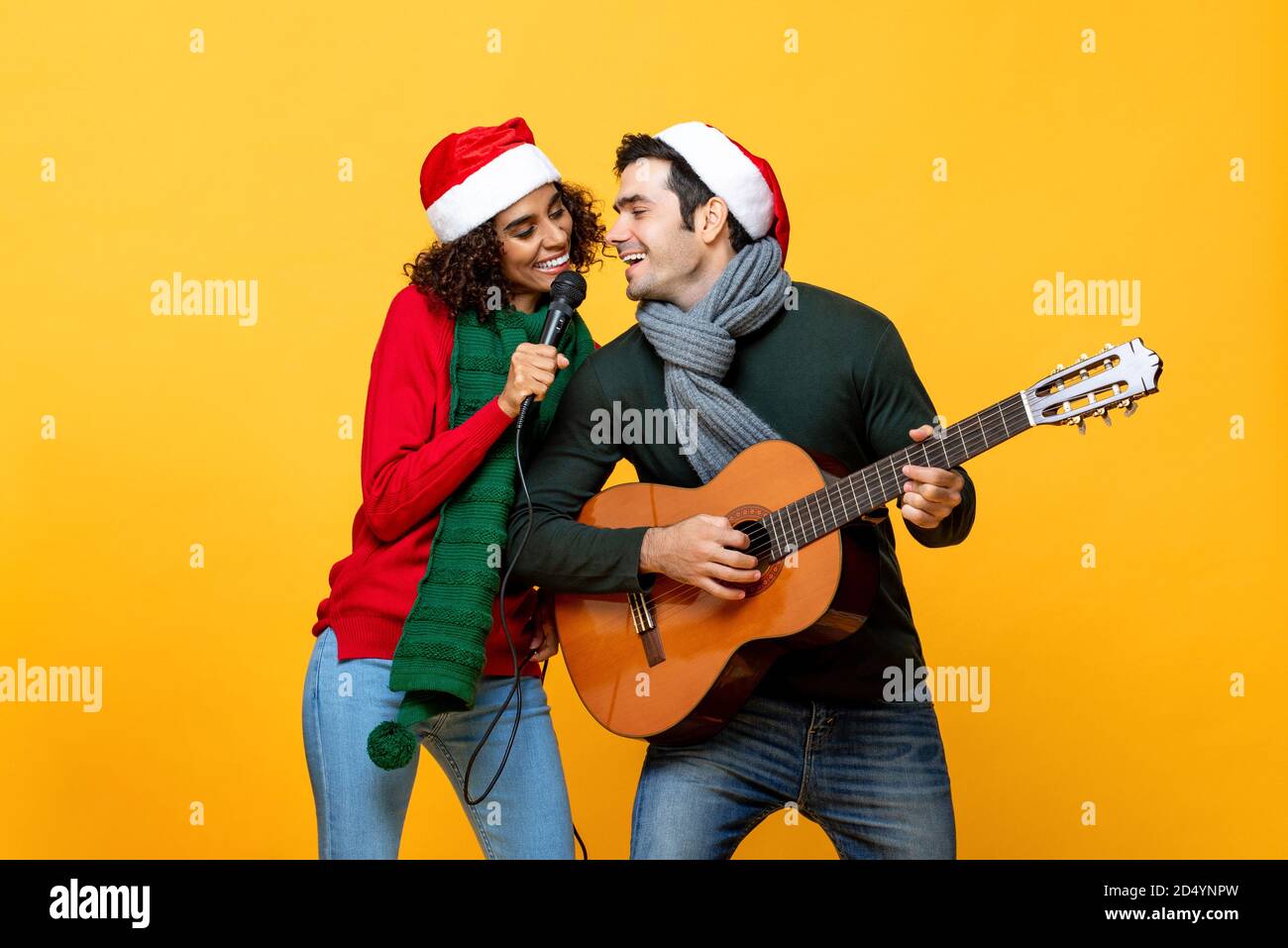 Felice coppia interracial cantare una canzone che celebra Natale in isolato sfondo giallo studio Foto Stock