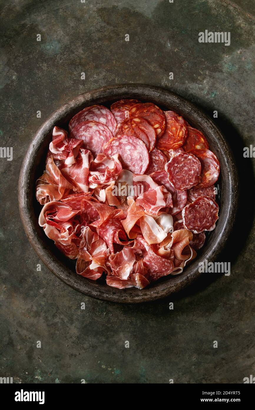 Antipasto piatto di carne assorti di fettine di prosciutto, salame, il salame chorizo in terracotta al di sopra del vassoio di metallo scuro dello sfondo. Laici piana, spazio Foto Stock