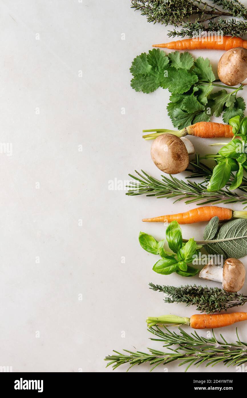 Varietà di cucina fresca erbe con mini carote e funghi champignon in fila su marmo bianco dello sfondo. Appartamento laico, spazio. Concetto di cucina a vista, cibo Foto Stock