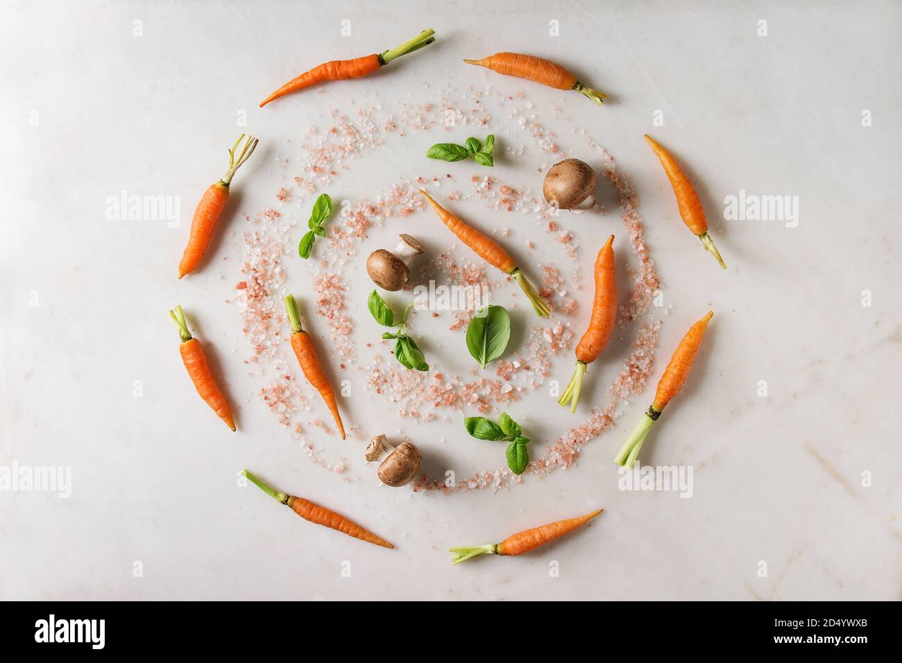 Il basilico fresco erbe con giovani mini carote, sale rosa e funghi champignon in spirale su marmo bianco dello sfondo. Appartamento laico, spazio. Concetto di cucina a vista Foto Stock