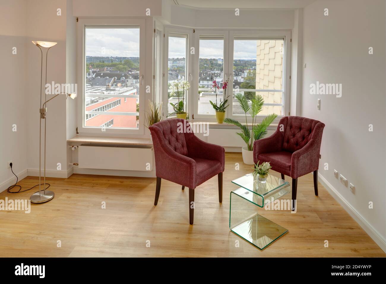 Appartamento mit Blick auf eine urbane Umgebung. In Front Eines grossen Fensters befindet sich eine 2er Sitzgruppe bestehend aus zwei roten Sesseln und e Foto Stock