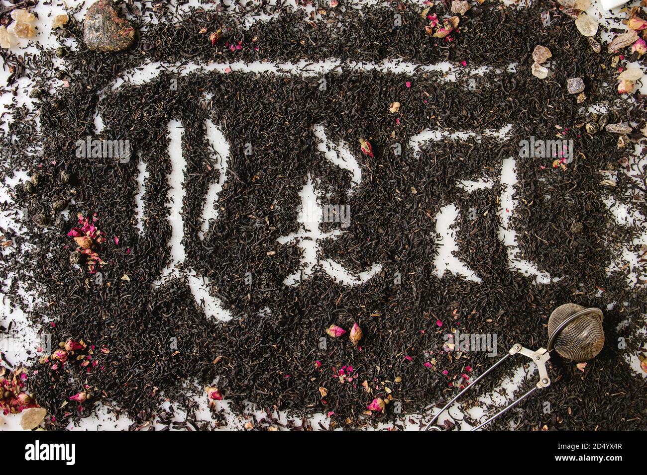 Iscrizione calligrafico lettere gotiche tè oltre a secco di ceylon nero e tè verde sparsi in marmo bianco con boccioli di rosa e stainer. Bere tè con Foto Stock