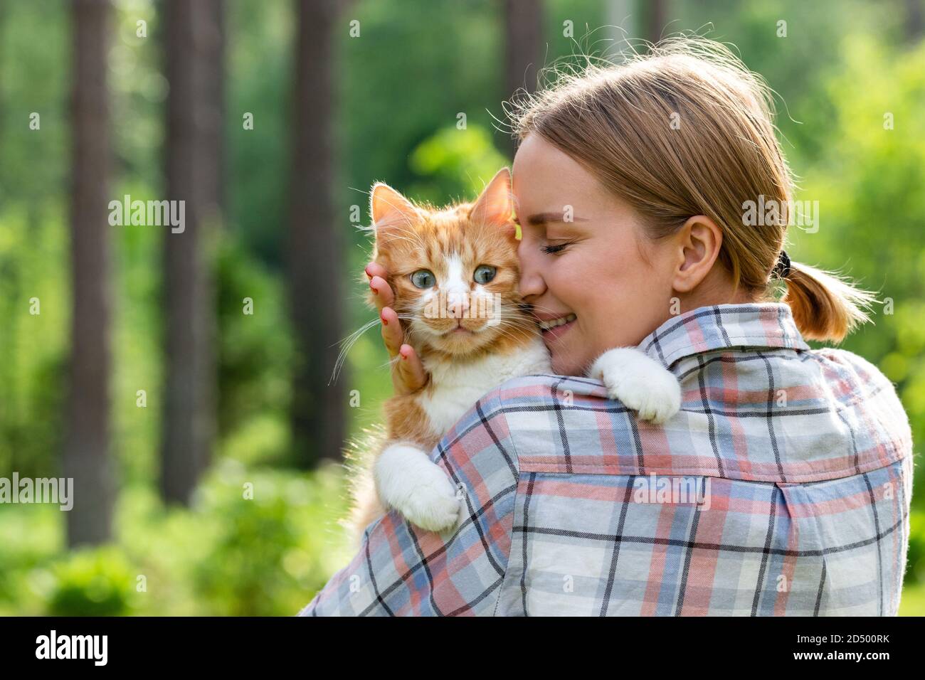 Primo piano di donna sorridente in camicia controllata abbracciando e abbracciando con tenerezza e amore domestico eccitato gatto triste all'aperto. Amore per gli animali, animali domestici Foto Stock