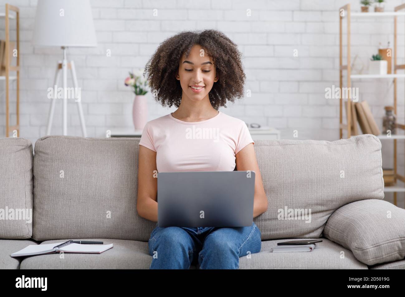 Navigare su Internet e cercare lavoro da casa. Donna afro-americana amichevole che lavora al computer portatile Foto Stock