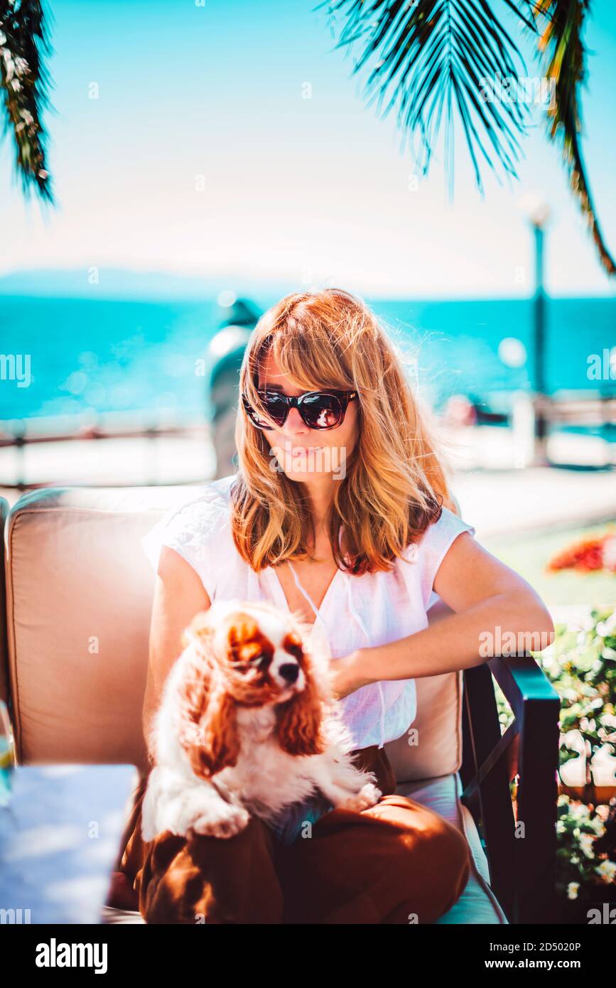 Foto di donna di mezza età godendo di una giornata di sole mentre si rilassa sul mare con il suo cucciolo di cavalier re charles. Foto Stock