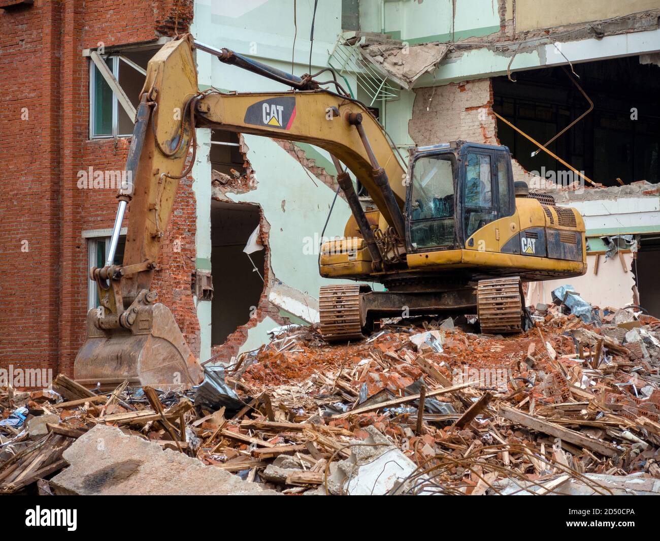 Escavatore giallo nel sito di demolizione, distrutto vecchio edificio in background Foto Stock