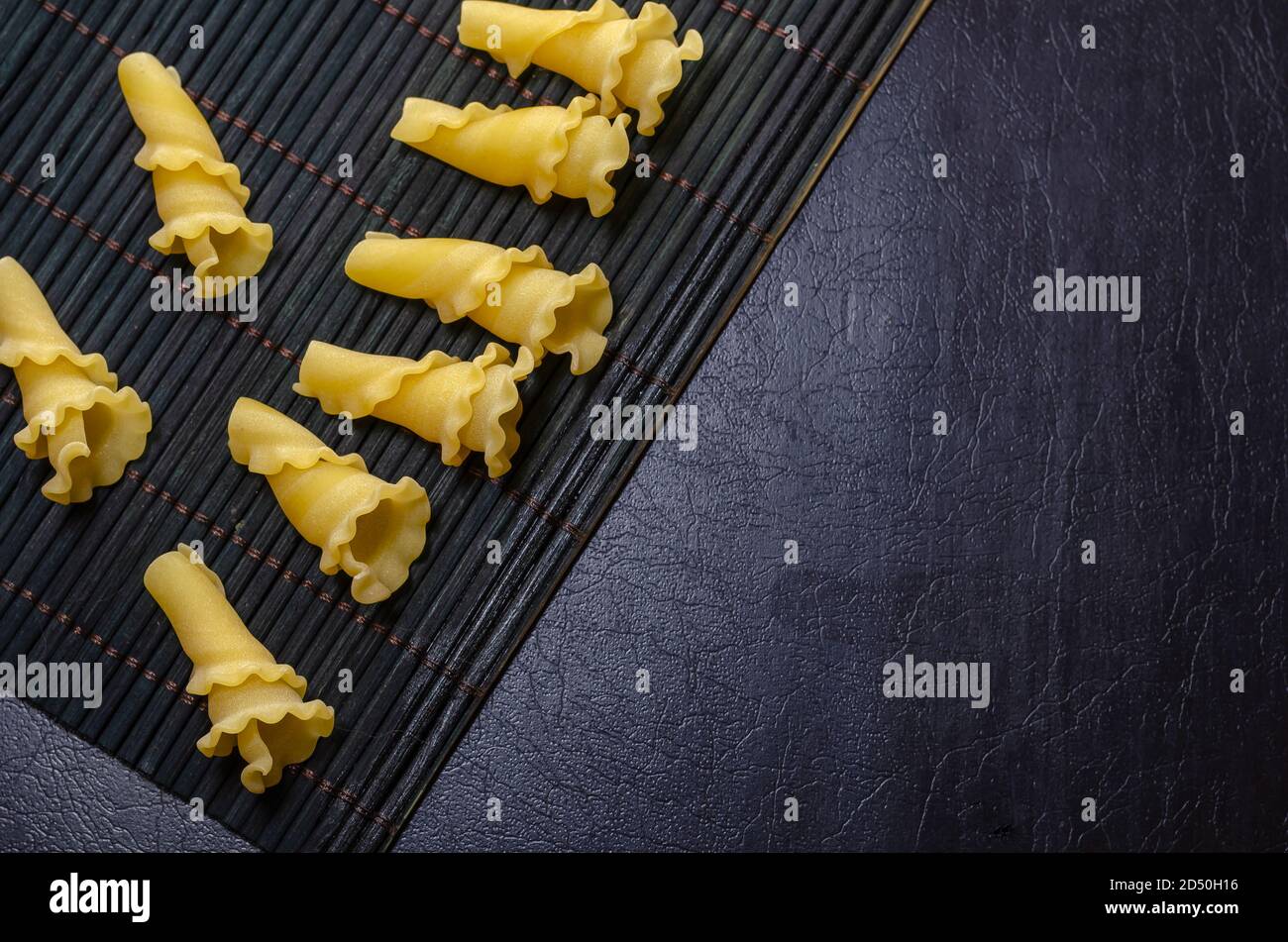 Gigli non cotti o campanelle su un tovagliolo di bambù scuro. Varietà di pasta italiana. Cucina mediterranea tradizionale. Foto Stock