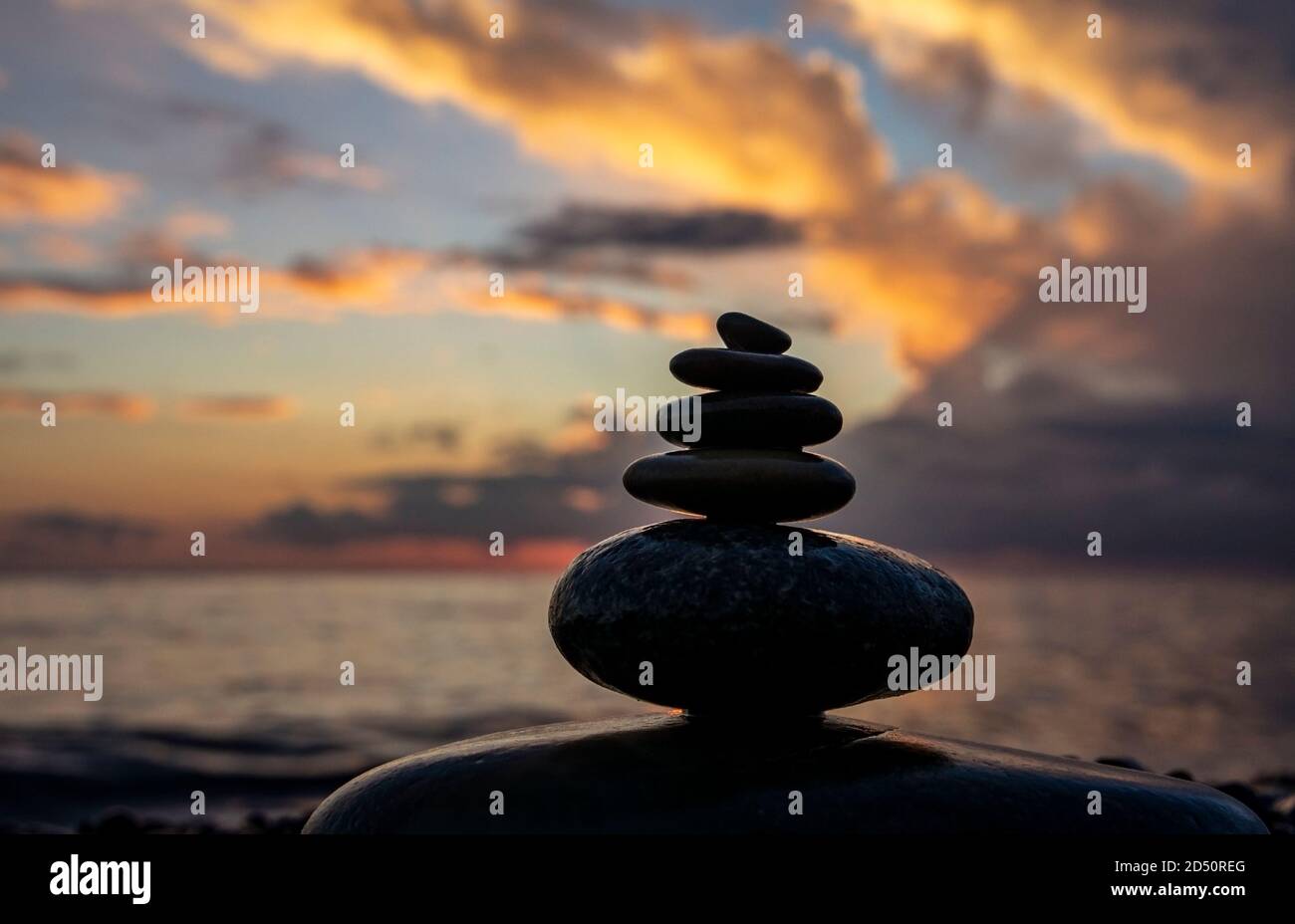 Pietre di ciottoli impilate sullo sfondo di un cielo nuvoloso luminoso al tramonto e al mare. Zen piramide ciottoli, sfondo Foto Stock