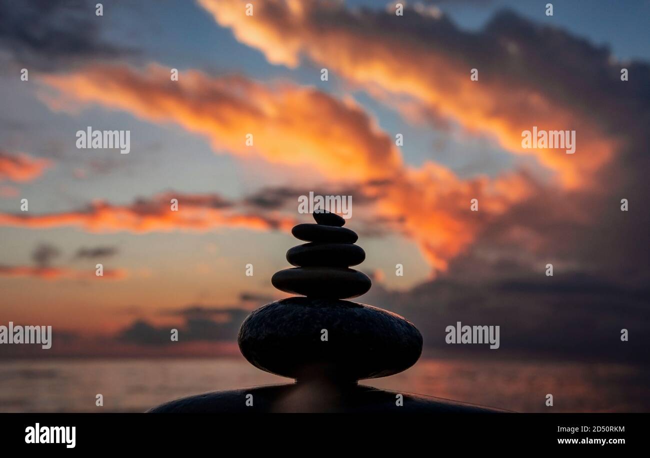 Pietre di ciottoli impilate sullo sfondo di un cielo nuvoloso luminoso al tramonto e al mare. Zen piramide ciottoli, sfondo, equilibrio e meditazione concetto Foto Stock