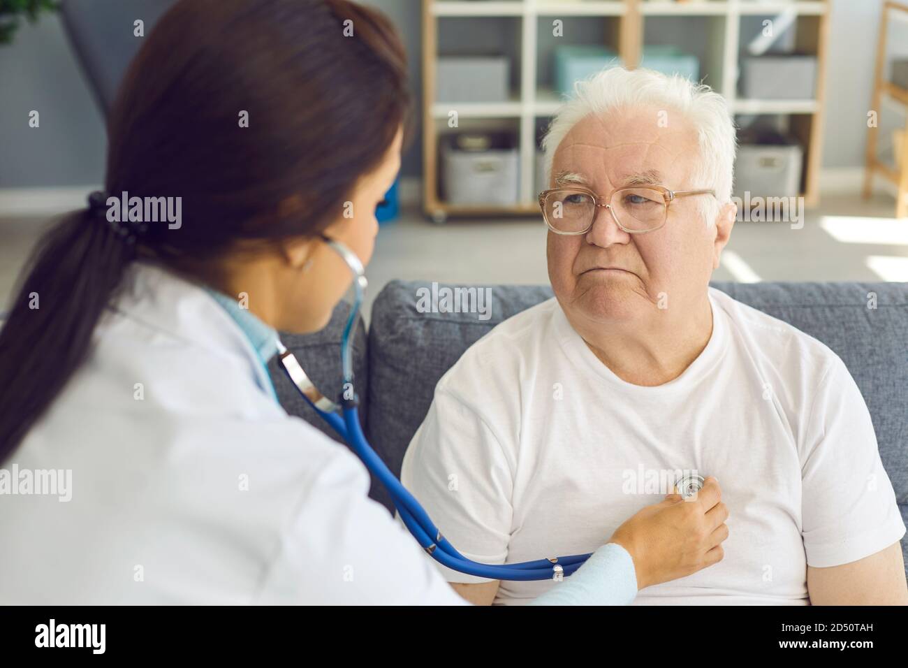 Medico femminile che ascolta il cuore del paziente maschio dai capelli bianchi attraverso lo stetoscopio Foto Stock