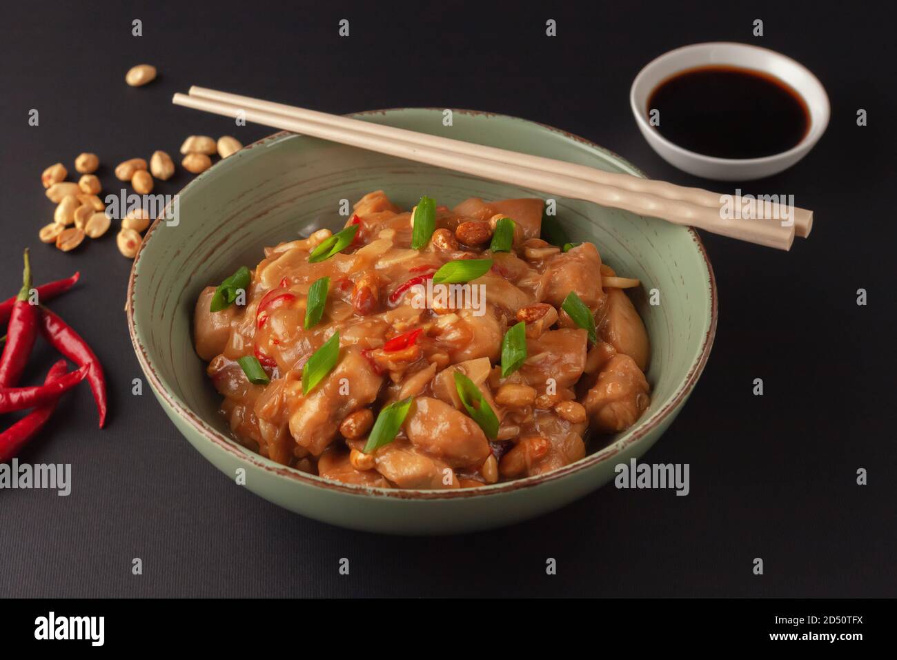 Pollo Kung Bao su sfondo nero. Un piatto cinese con pollo, peperoncino, arachidi, salse e cipolle. Foto Stock