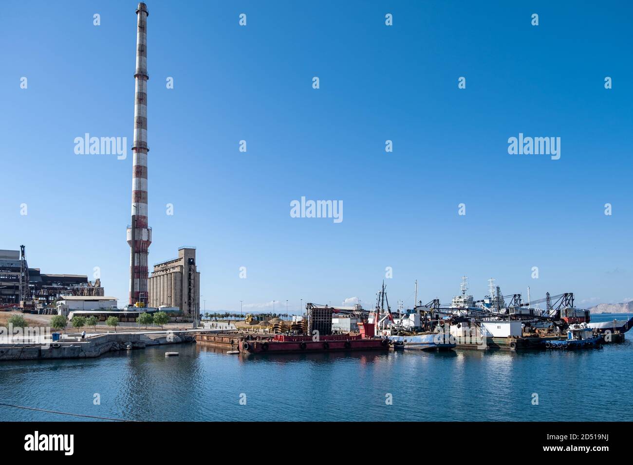 Vecchio stabilimento industriale abbandonato e barche ancorate al porto. Rovine della fabbrica di fertilizzanti a Drapetsona Pireo Grecia, cielo blu e mare, soleggiata da Foto Stock