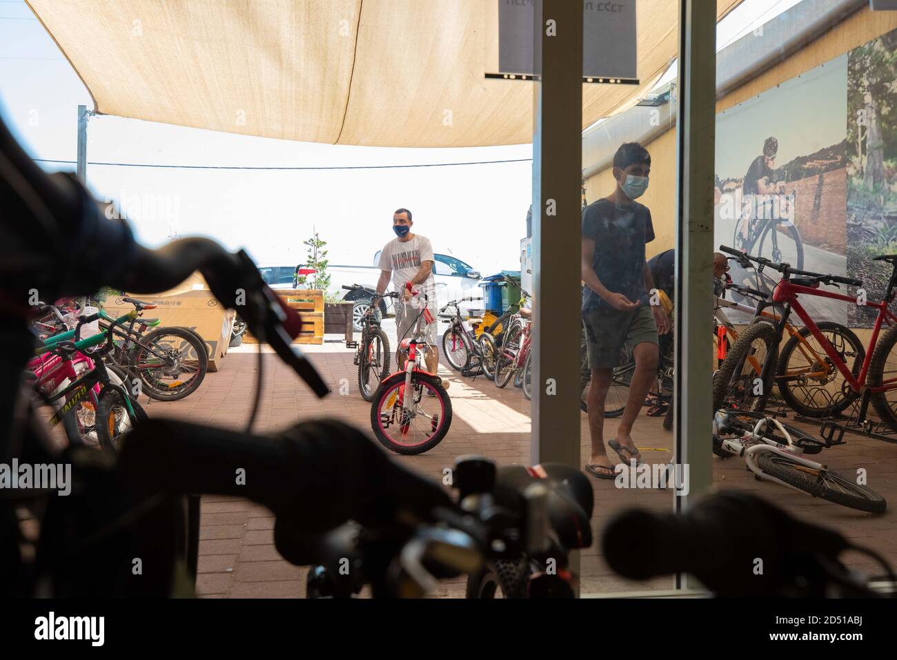 Negozio di biciclette durante il COVID-19 Pandemic. I clienti aspettano fuori dal piccolo negozio per il servizio e vengono serviti alla porta. I clienti sono obbligati a wea Foto Stock