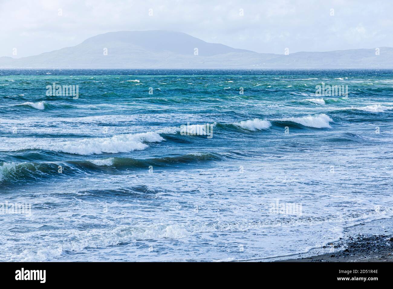 Onde che rotolano verso la riva in una giornata ventosa in Clew Bay con vista sull'isola di Clare dalla pietra spiaggia a Killadoon sul giro di Killeen passeggiate vicino Louis Foto Stock