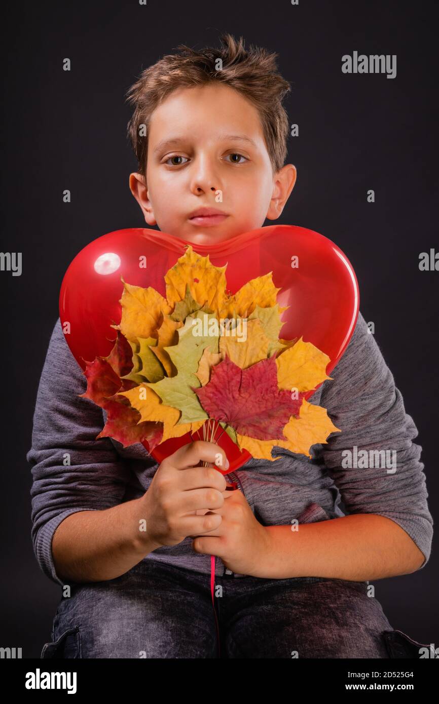 Ragazzo che ama l'autunno con un pallone a forma di cuore e colore autunno foglie di acero Foto Stock