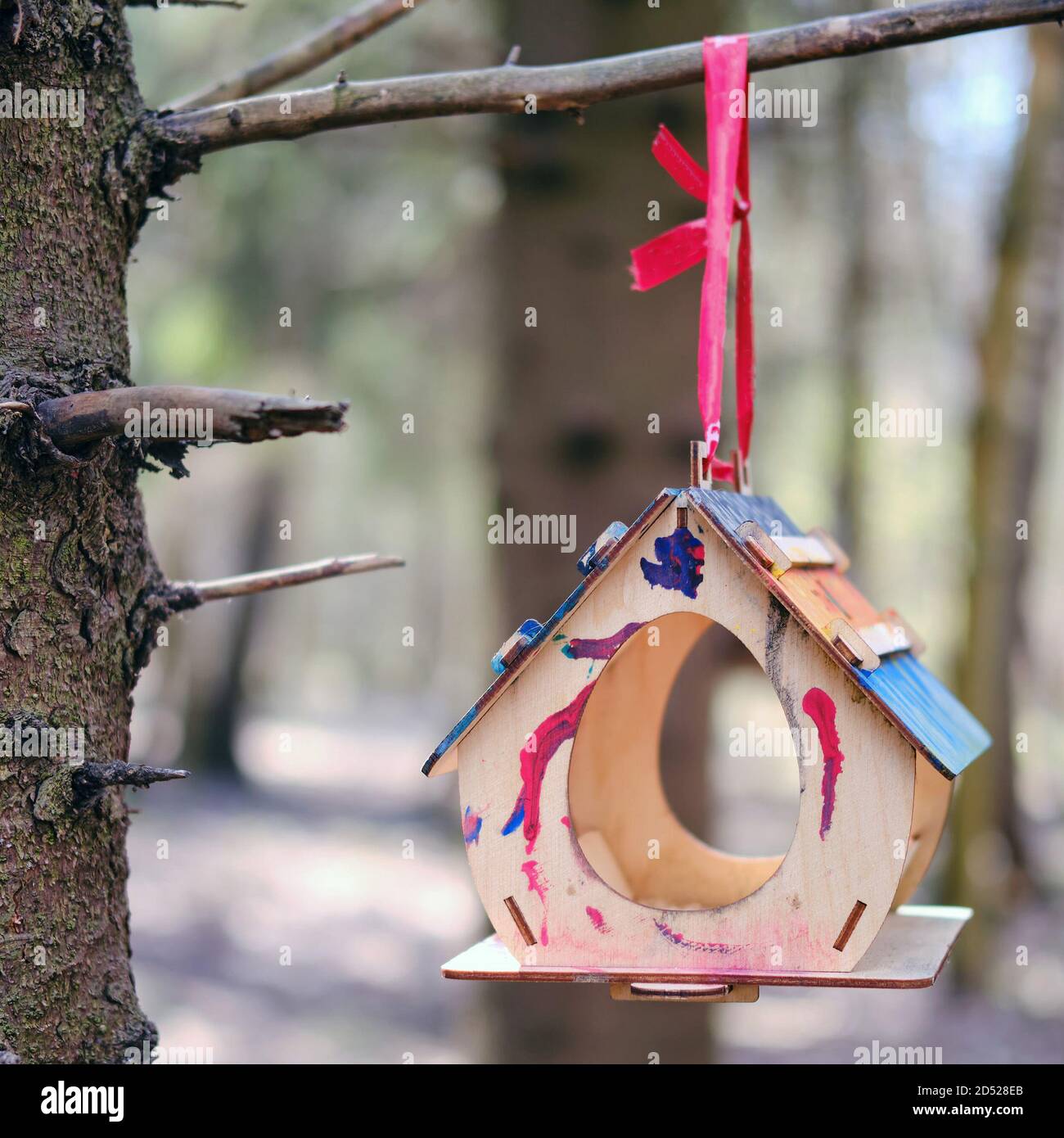 Un alimentatore di legno con macchie di vernice multicolore è sospeso un albero nel parco Foto Stock