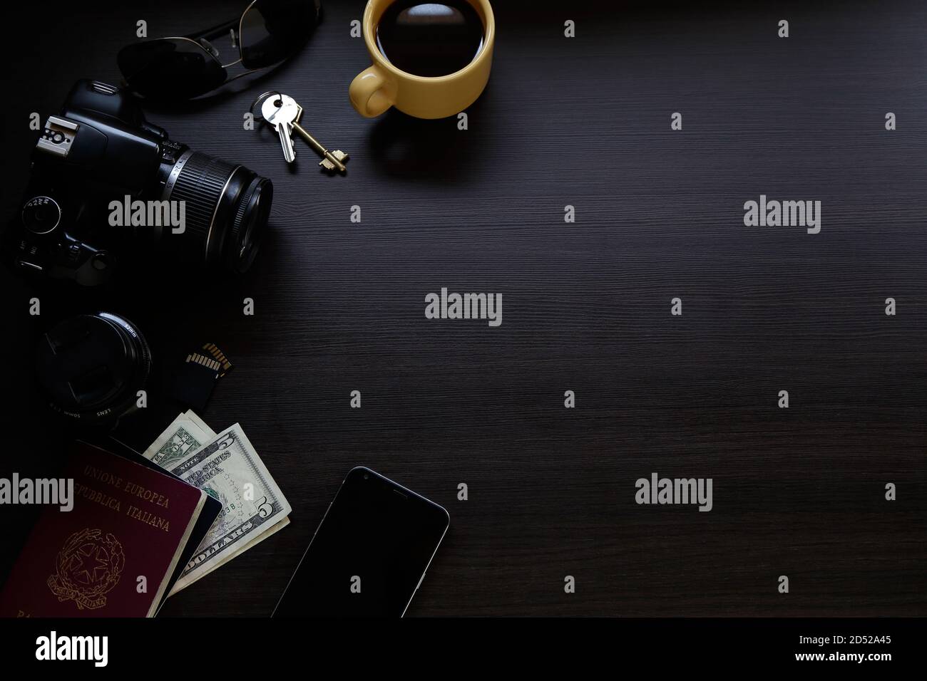 Vista dall'alto della scrivania in legno scuro con fotocamera digitale reflex, uno smartphone, passaporto, chiavi, caffè e denaro. Spazio di copia. Foto Stock