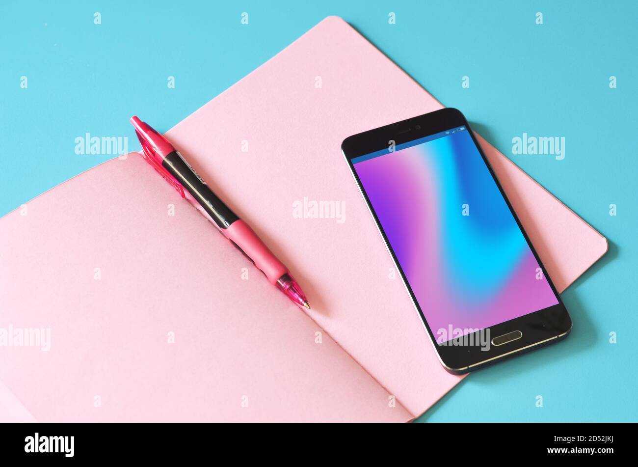 Smartphone e notebook rosa su tavolo blu. Foto Stock