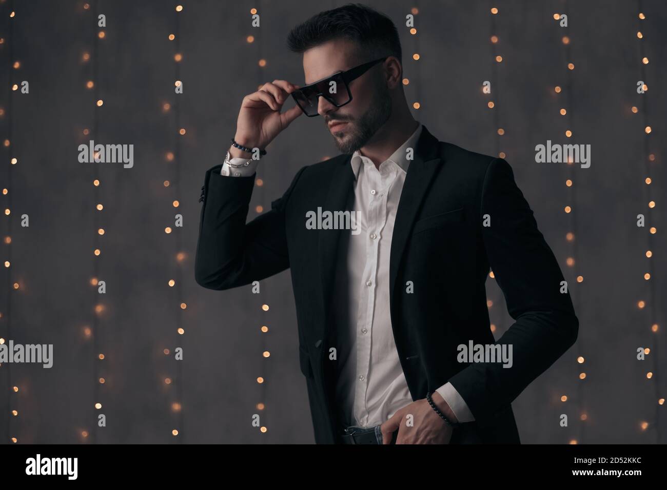 Modello di moda sicuro togliere i suoi occhiali da sole e guardare via mentre si sta in piedi su sfondo grigio studio con luci Foto Stock