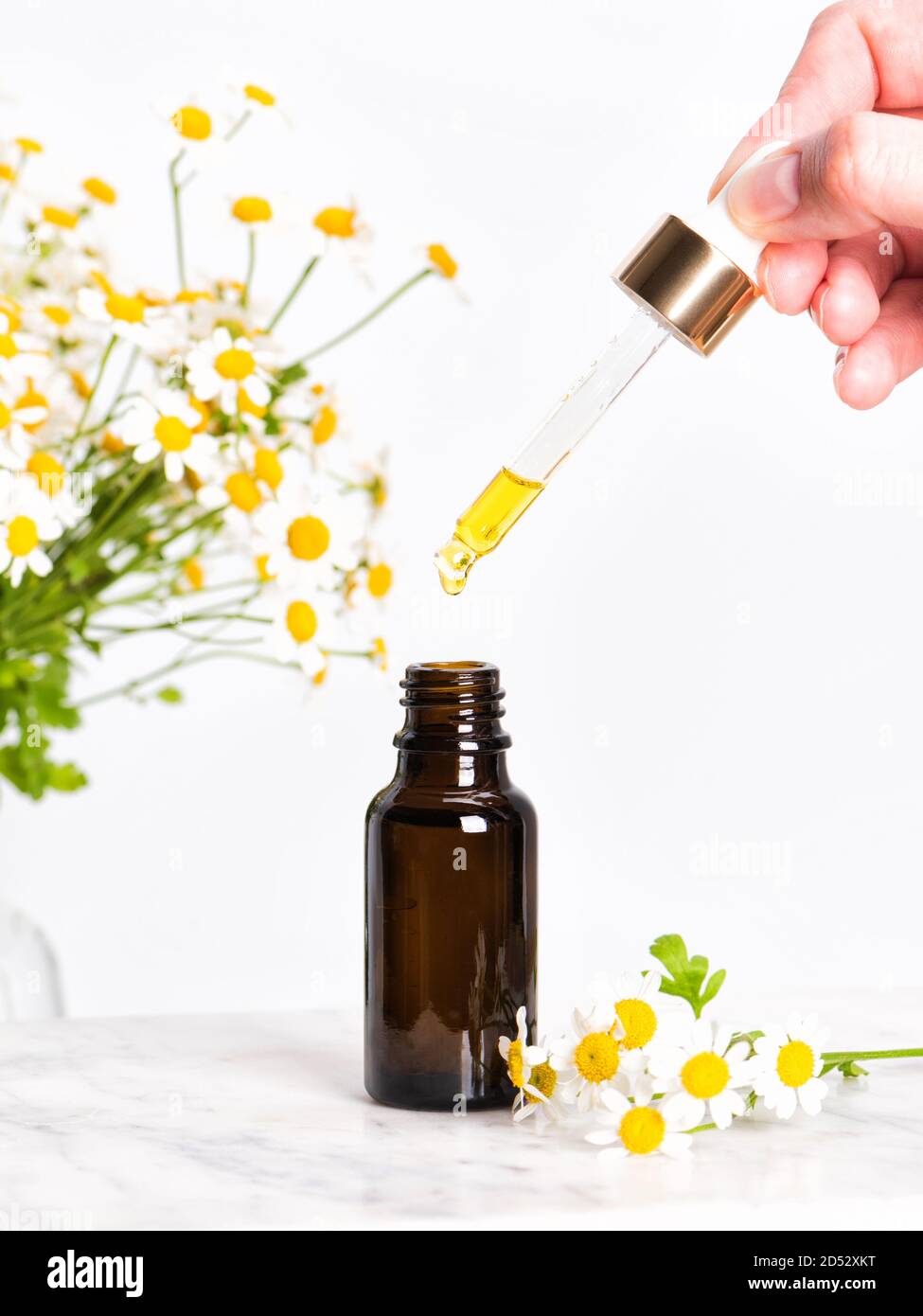 Bottiglia di essenza o siero di vetro marrone con camomilla fiori Foto Stock