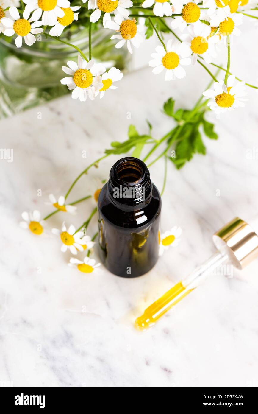 Bottiglia di essenza o siero di vetro marrone con camomilla fiori Foto Stock