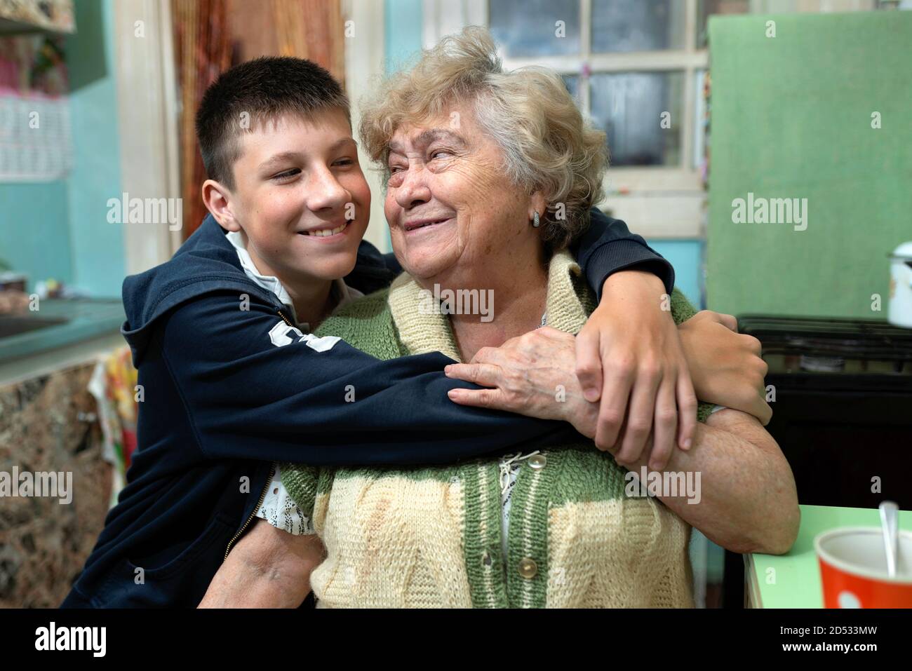 Nonna e nipote felici si abbracciano in cucina a casa. Relazioni intergenerazionali, valori familiari, amore, cura. Povero, peopl ordinario Foto Stock