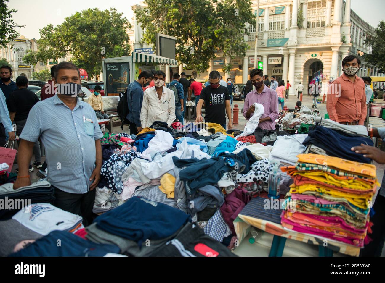 Un venditore di vestiti locale è visto indossare un facemask mentre si sta in piedi accanto alla sua sezione di vestiti sul lato della strada del mercato Connaught Place. Il governo ha adottato misure sostanziali per la ripresa dell'economia indiana. La gente ha cominciato uscire dalle loro case per fare gli acquisti. Il trambusto del mercato mostra che l'economia si sta gradualmente muovendo verso la ripresa. Foto Stock