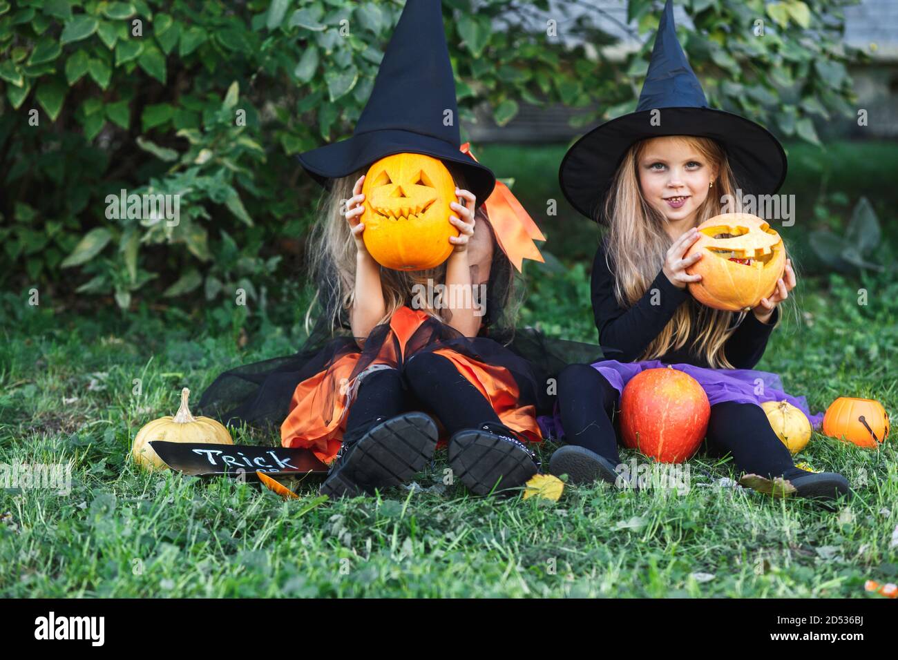 Felice Halloween. Due bambini divertenti in abiti da strega e con zucche sedute all'aperto Foto Stock