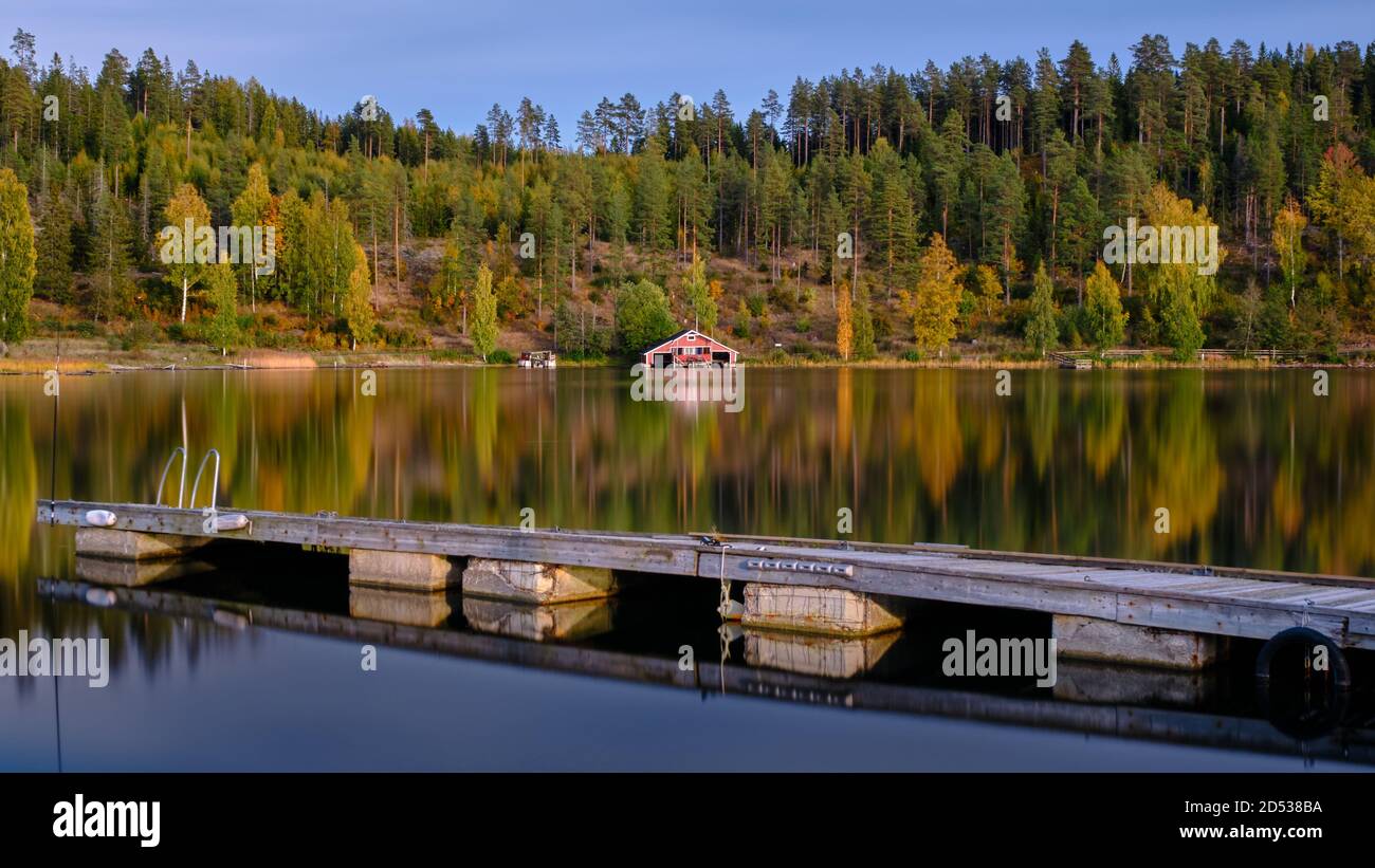 Jetty in primo piano e una boathouse rossa e la foresta in autunno colori sullo sfondo Foto Stock