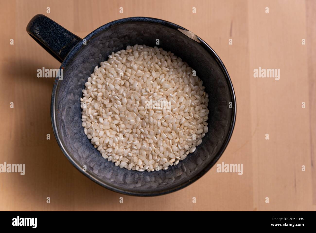 vista dall'alto della ciotola blu di riso crudo bianco non fatto su tavola di legno. il riso è un alimento di base e una base per l'alimentazione e la dieta di molta gente Foto Stock