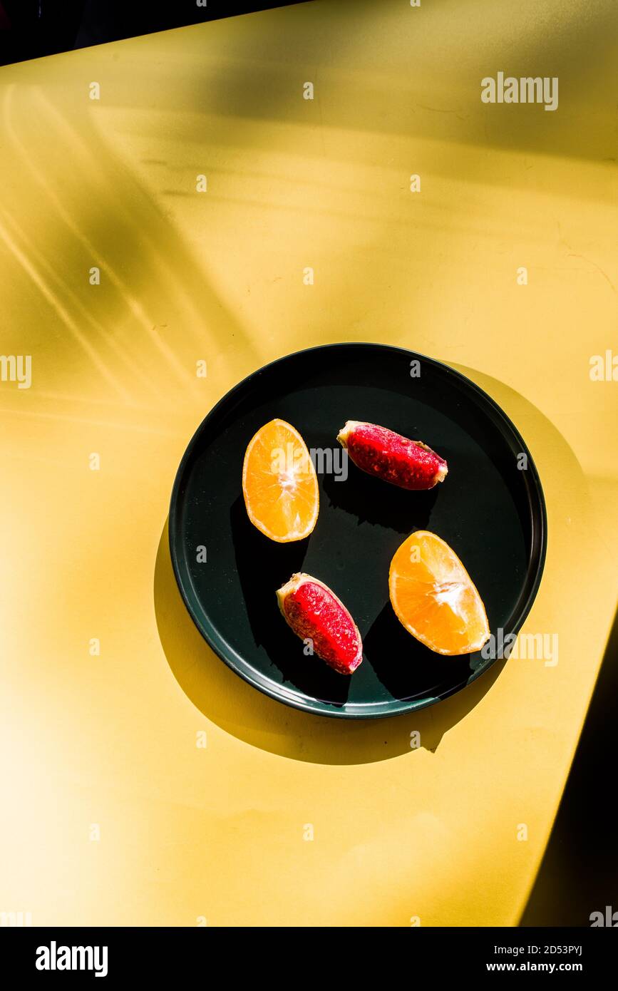 Prickly Pere frutta e arancia su un piatto scuro su uno sfondo giallo pannello, un po 'di ombra su di esso Foto Stock