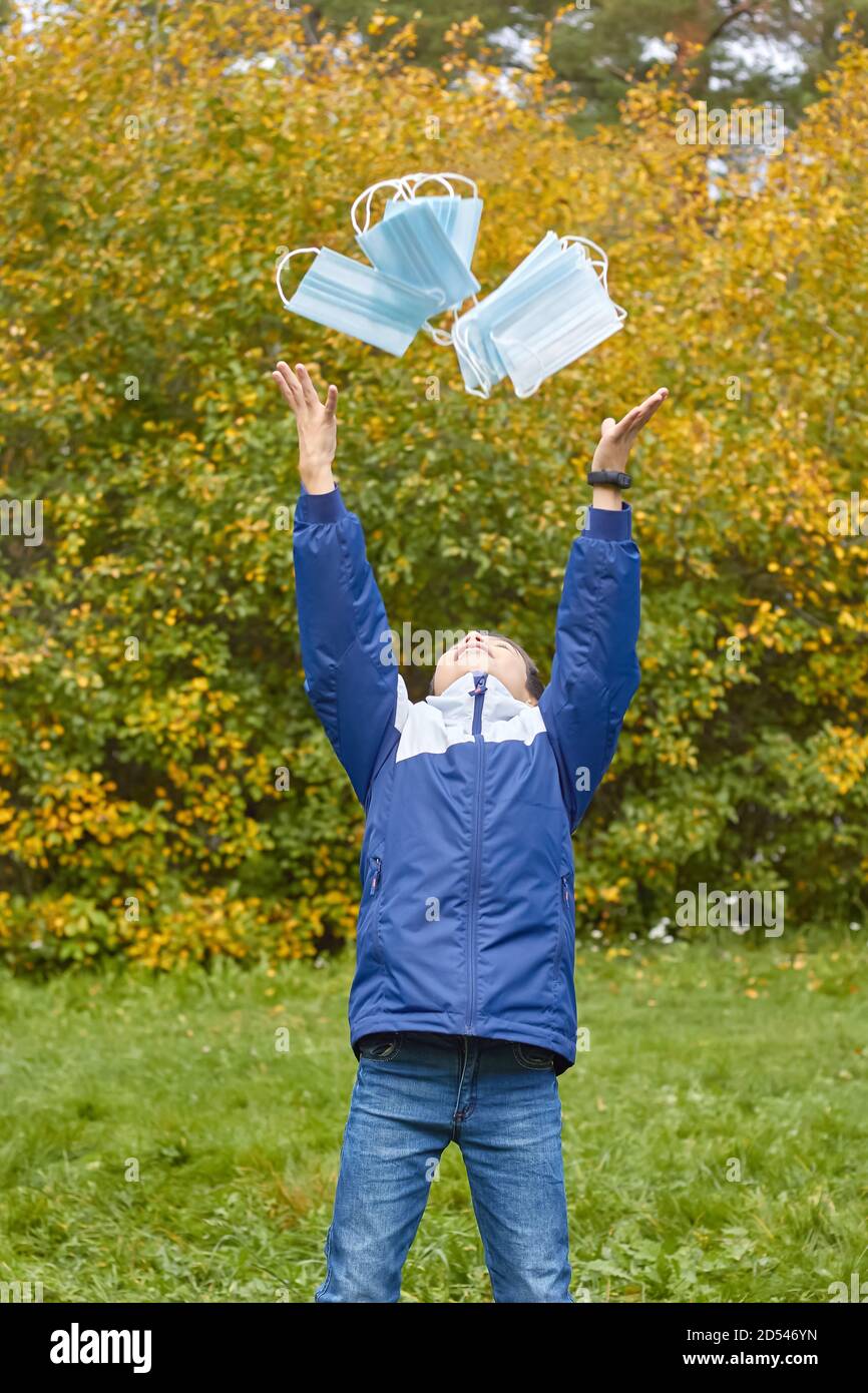 Giovane ragazzo in parco in autunno tra foglie gialle che si lanciano maschere mediche monouso Foto Stock