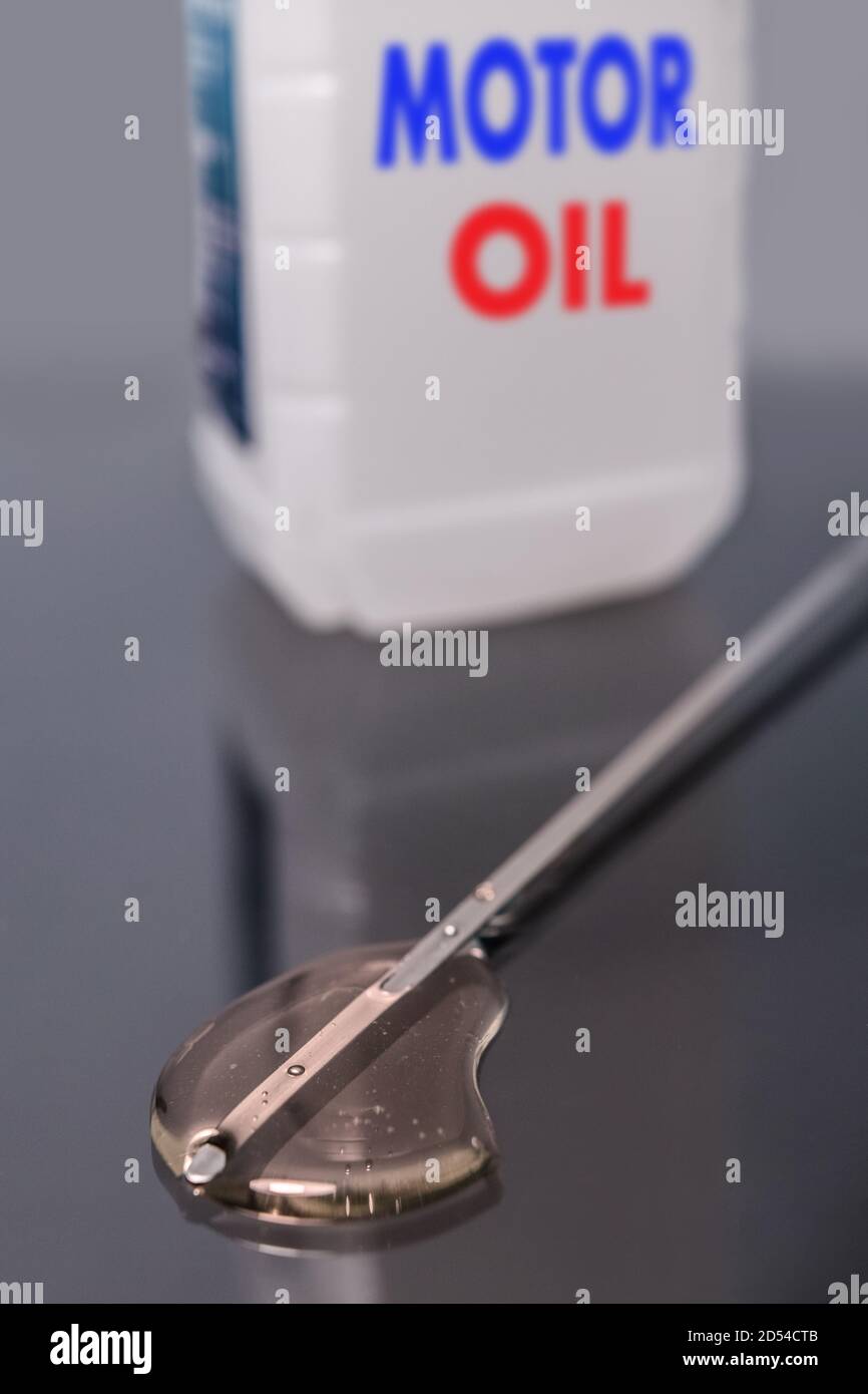 La punta dell'astina di livello e il gocciolamento di olio. Sullo sfondo vediamo una bottiglia di olio motore. Foto Stock