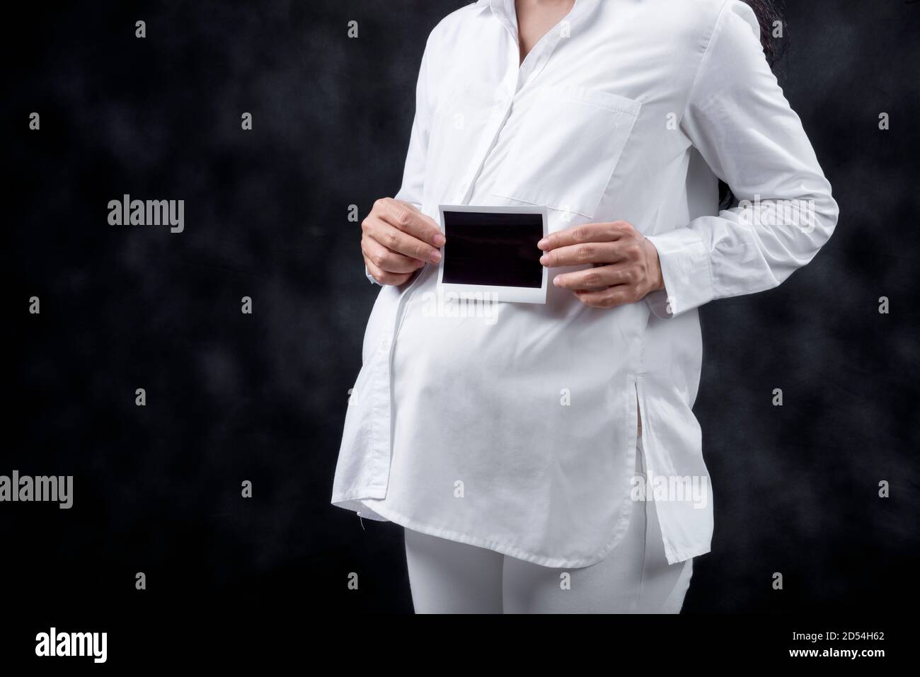 Donna incinta che tiene ecograficamente il risultato del test di gravidanza con fondo nero Foto Stock