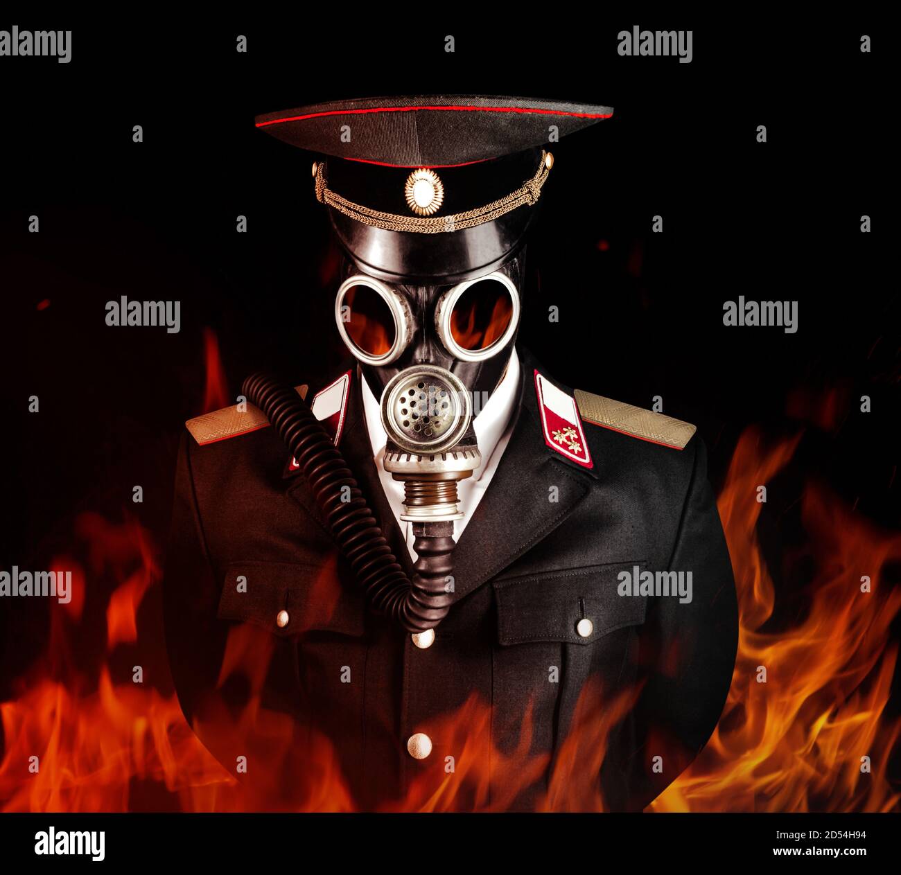 Foto di un ufficiale militare post-apocalittico in tuta uniforme e tappo a picco in piedi nella maschera a gas sovietica nel fuoco. Foto Stock