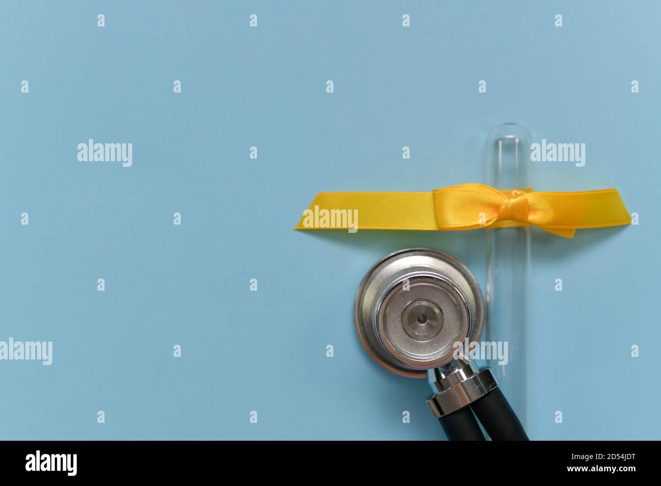 Una membrana di stetoscopio rotonda accanto a una provetta di vetro rovesciata vuota con un arco giallo in treccia a nastro satinato. Foto Stock